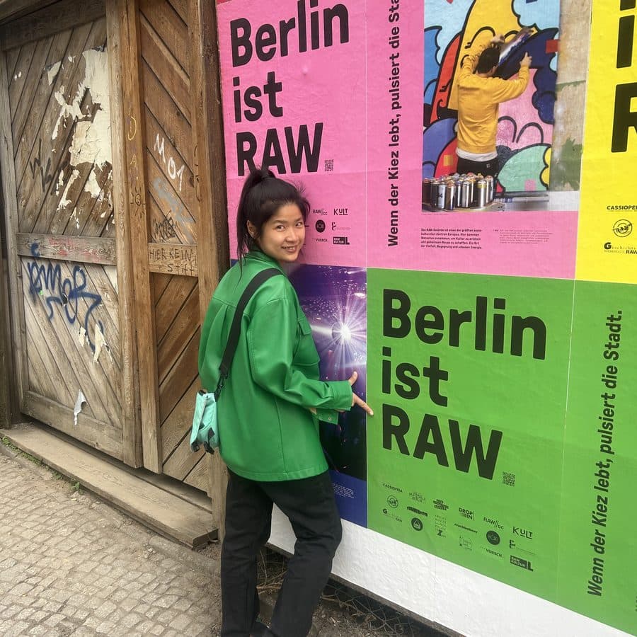 Shirley in a green jacket in front of pink and green Berlin street posters