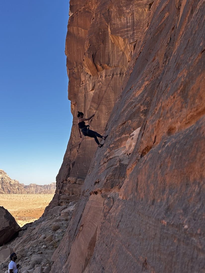A climber high on the underside of an overhanging desert arch