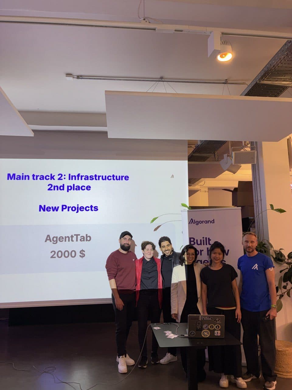The AgentTab team on the hackathon stage, the screen reading Main track 2: Infrastructure, 2nd place, AgentTab, $2,000